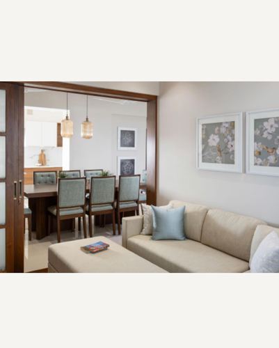 Beige living room sofa with sage cushion, opening through glass sliding door to dining area with pendant lights