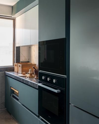 Muted teal kitchen cabinetry with built-in black oven and microwave beside window
