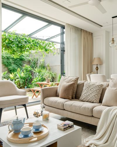 Beige living room with sofa, tea tray, and glass wall opening to a green courtyard