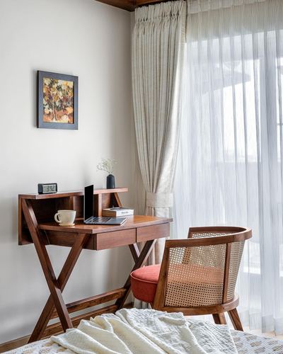Wooden writing desk with cane chair beside sheer curtained window in bedroom corner