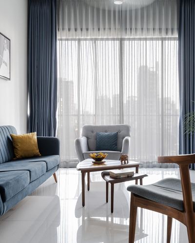 Living room with blue sofa, grey armchair, wood coffee table, sheer curtains and city view