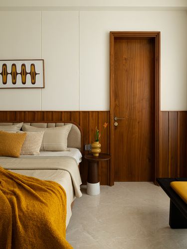 Bedroom with fluted wood wainscoting, matching timber door, and mustard-accented bedding on marble-look floor