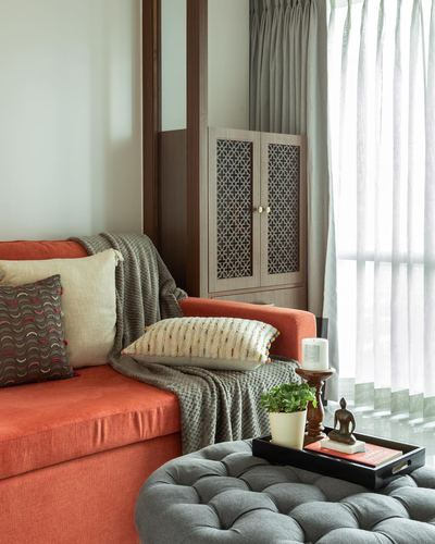 Orange velvet sofa with cushions beside a jali cabinet and sheer curtained window in a Mumbai apartment