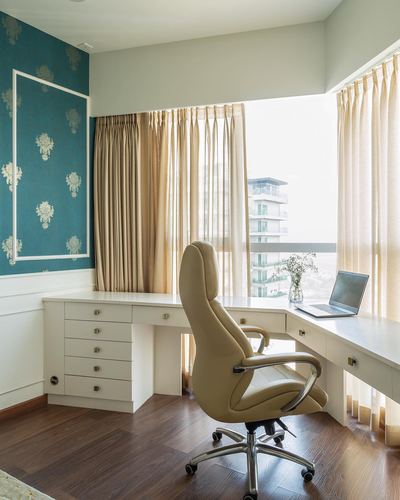 Corner home office with L-shaped white desk, cream leather chair, and teal wallpaper accent wall