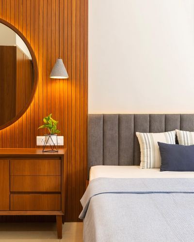 Bedroom corner with wood-panelled wall, round mirror, cone pendant light and grey channel headboard