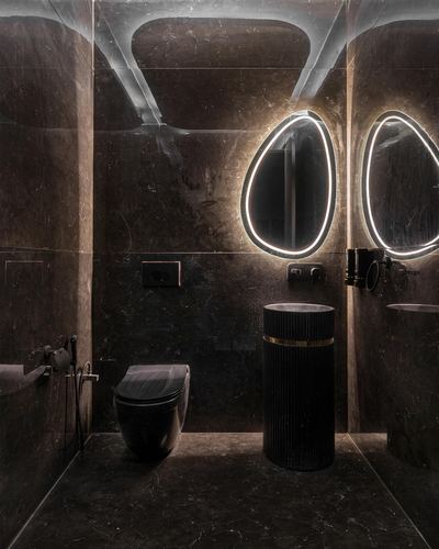 Dark stone bathroom with two egg-shaped backlit mirrors and a fluted pedestal basin
