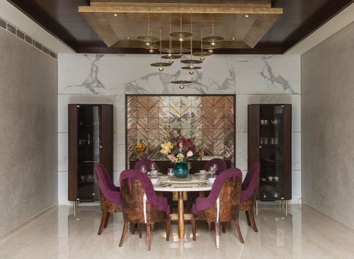 Symmetrical dining room with purple velvet chairs, marble-top table, herringbone panel and brass chandelier