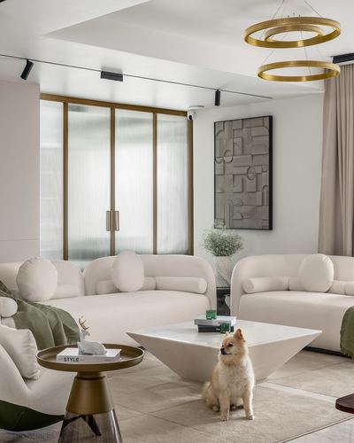 Cream living room with boucle sofas, marble coffee table, brass ring pendants, and a dog on the rug