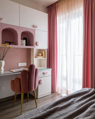 Pink and white study nook with scalloped velvet chair beside curtained window