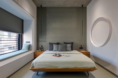 Minimalist bedroom with wood bed, ribbed grey headboard wall, window seat, and circular wall niche
