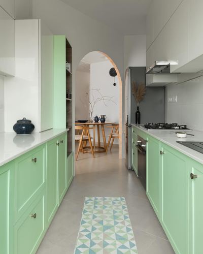 Mint-green galley kitchen with white countertops leading through an arch to a dining area