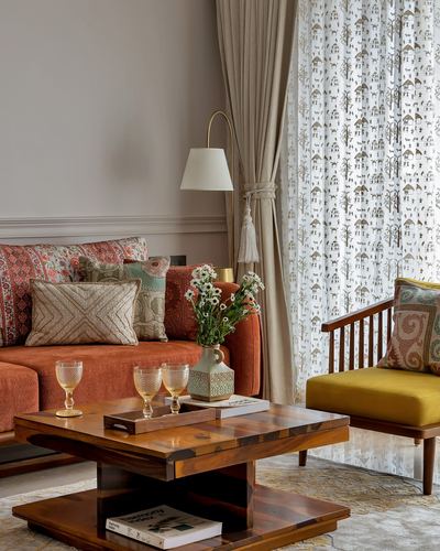 Living room corner with terracotta sofa, mustard chair, wooden coffee table and sheer printed curtains