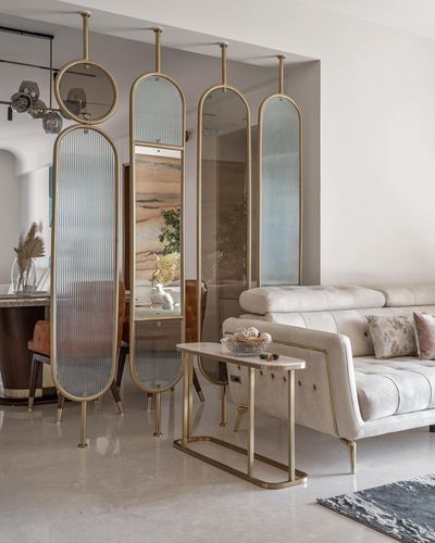 Living room with brass-framed hanging mirrors dividing space from dining area, beige tufted sofa and marble console