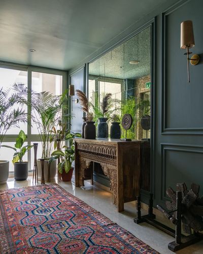 Green-paneled foyer with mirrored wall, carved wood console, plants and a patterned rug