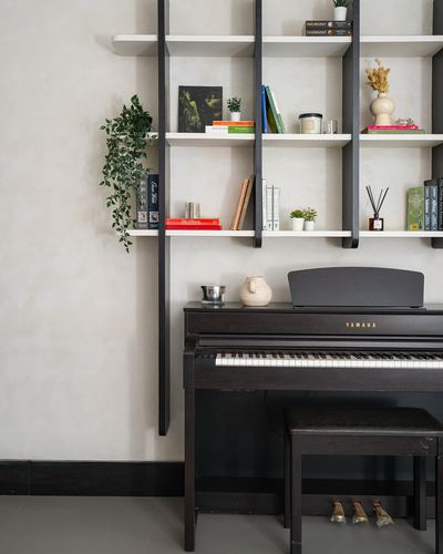 Black upright digital piano beneath a black-framed wall shelving unit with books and plants