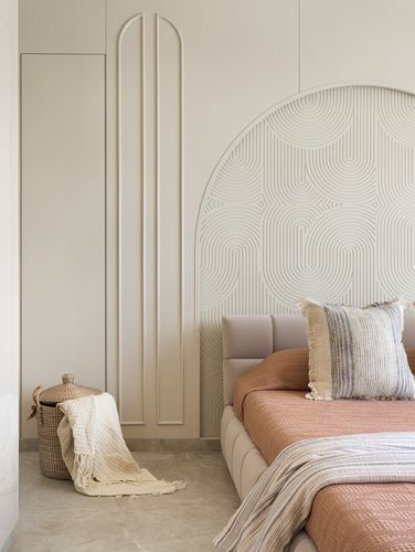 Bedroom corner with carved arch headboard wall, terracotta bedding, and a woven basket beside fluted panelling.
