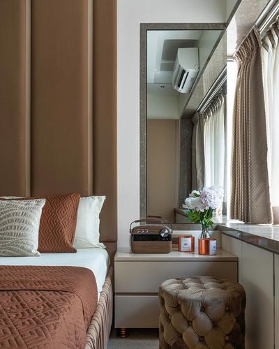 Bedroom nook with tan leather headboard, mirrored vanity table, and tufted velvet ottoman