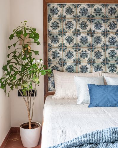 Bedroom corner with potted plant beside a bed framed by a blue floral tile headboard