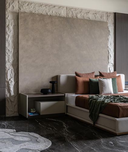 Bedroom with textured stone-framed plaster wall, terracotta and green bedding, dark marble floor