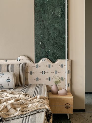 Bedroom corner with scalloped patterned headboard beside a green marble wall panel and wooden nightstand