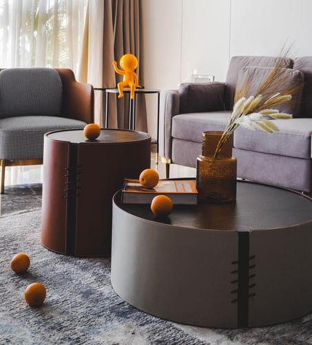 Two round leather drum coffee tables with oranges and a vase in a grey velvet living room