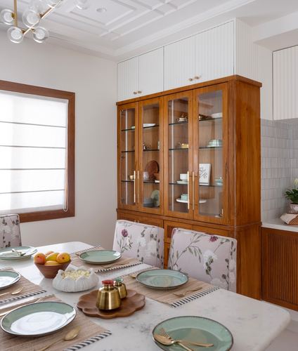 Dining room with marble-top table, floral chairs, and a tall wooden glass-front crockery cabinet.