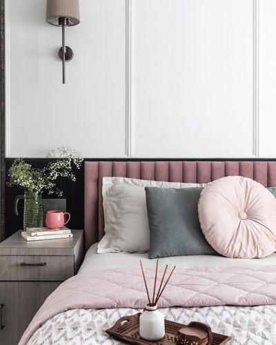 Bed with pink channel-tufted headboard, layered cushions, and styled wooden nightstand with wall sconce.