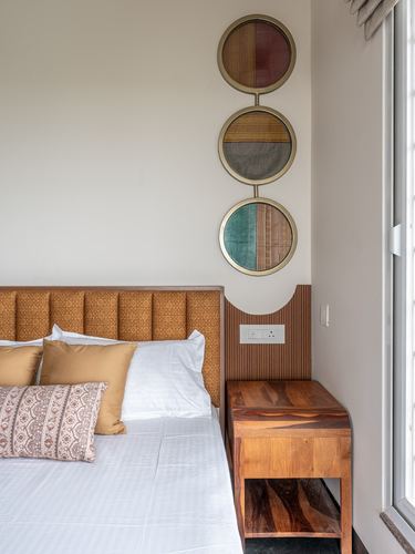 Bedroom corner with mustard quilted headboard, round textile art, and a sculpted wooden nightstand