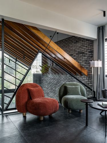 Two rounded boucle chairs, rust and sage, beneath an angular wood-slat staircase and brick wall