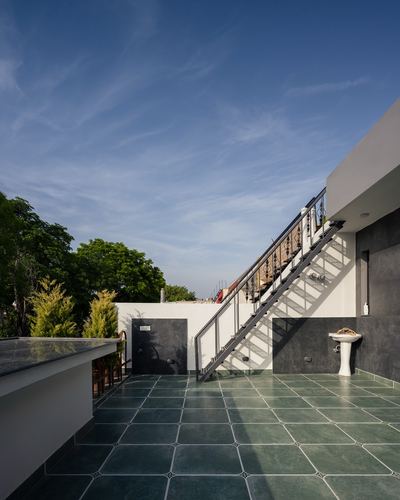 Rooftop terrace with green stone tile flooring, steel staircase, and pedestal basin under blue sky