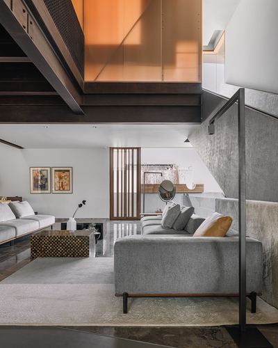 Double-height living room with steel bridge overhead, grey sofas, and amber glass accent above