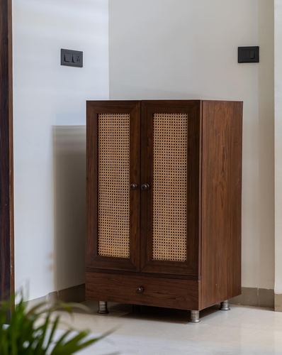 Dark wood cupboard with cane-panel doors and drawer in a corner niche