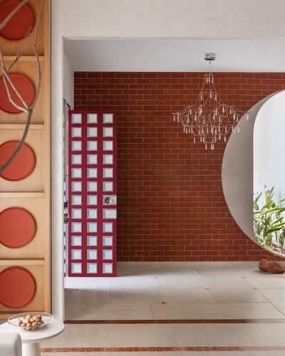 Foyer with red brick wall, magenta grid door, chandelier and circular opening to garden