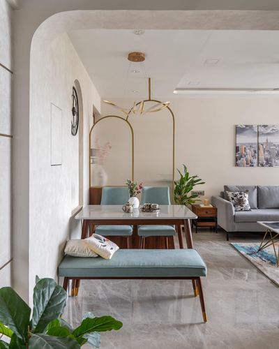Dining nook with blue velvet chairs, marble table, and sculptural gold pendant light, opening to living room