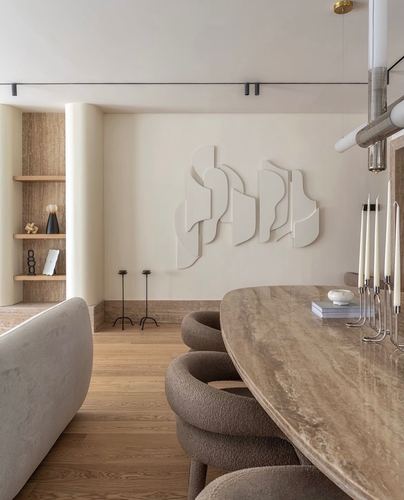 Curved bouclé dining chairs around a stone oval table beneath a sculptural wall relief