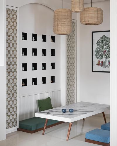 Dining nook with niche wall of vases, rattan pendant lights, and marble-top table on wooden legs