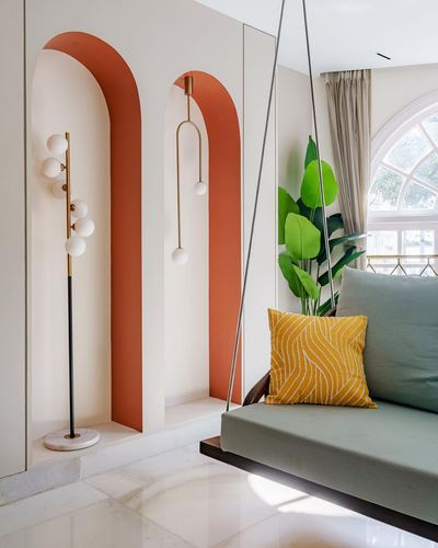 Terracotta arched niches with brass globe lamps beside a green swing daybed and marble floor