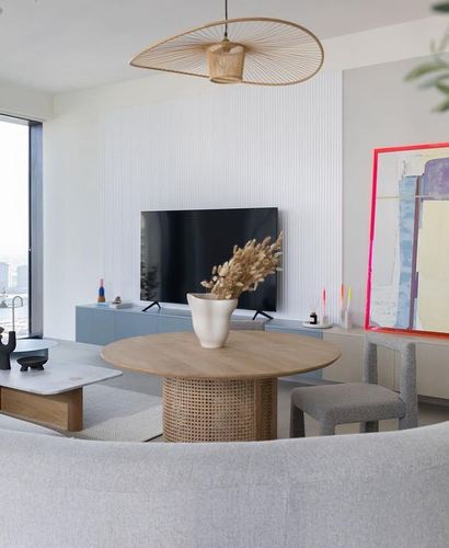 Open living-dining space with cane-base wood table, woven pendant light, and fluted TV wall panel