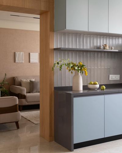 Kitchen counter with blue cabinets, ribbed tile backsplash, vase of yellow flowers, view into living room