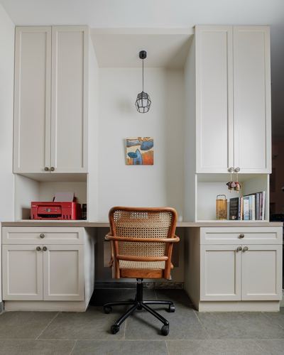 Built-in white desk nook with cane chair, pendant light, and small artwork in a study