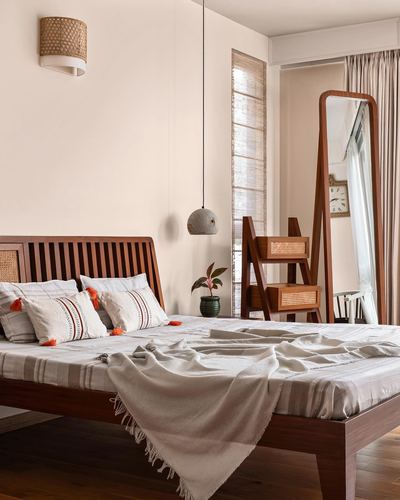 Bedroom with slatted wood bed, striped linens, cane wall sconce, and standing mirror beside window