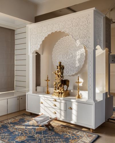 White carved pooja unit with arched niche, brass Krishna idol, and diyas above a drawer cabinet on a blue rug