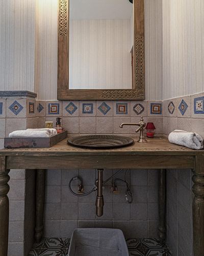 Bathroom vanity with carved wood mirror, brass vessel sink and patterned tile backsplash