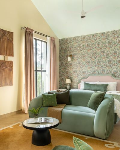 Bedroom with green floral wallpaper, pink headboard, curved green velvet sofa and mustard rug