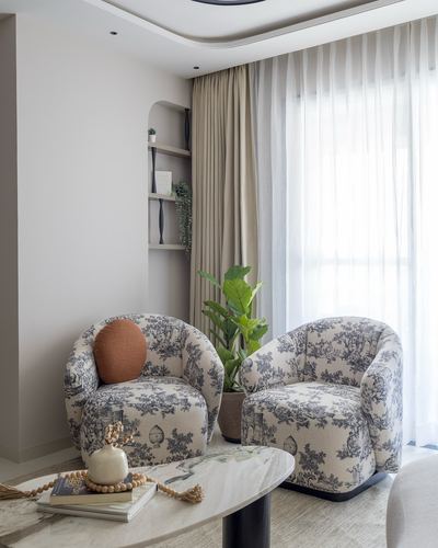 Two toile-print armchairs beside a marble coffee table near a curtained window