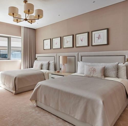 Twin beds with pink upholstered headboards beneath five framed botanical prints in a blush pink bedroom