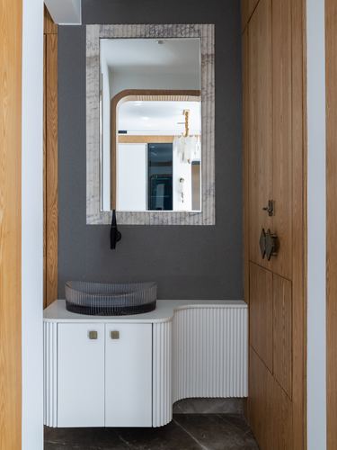 Bathroom vignette with ribbed mirror, glass vessel sink, and curved fluted white vanity against grey wall
