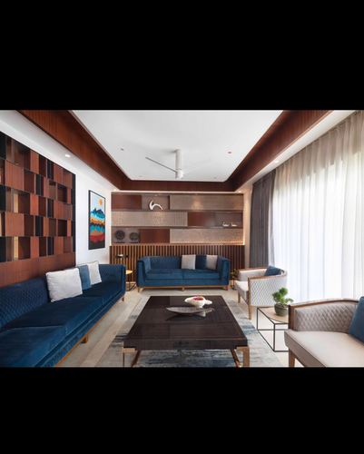 Living room with blue velvet sofas, dark wood coffered ceiling, and textured display shelving
