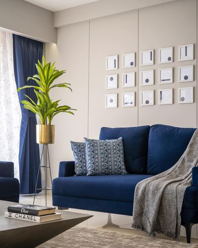 Navy velvet sofa against beige panelled wall with grid gallery art and brass planter