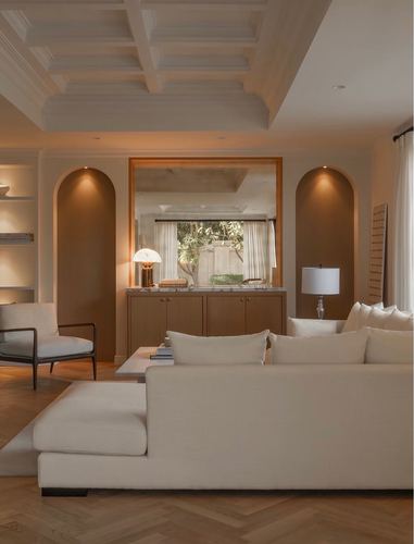 Cream living room with coffered ceiling, arched niches, and wood console beneath a window